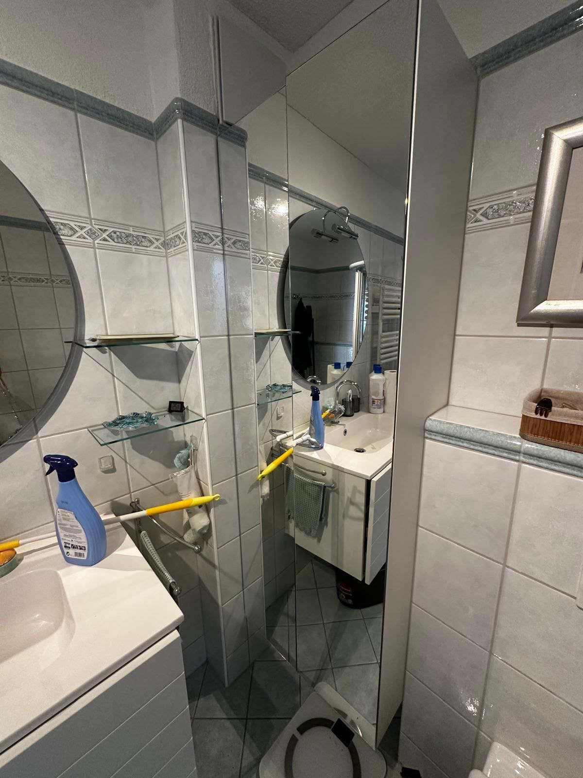Badezimmer vorher: alter Hochschrank mit Spiegeltür neben Lavabo und Glasablagen